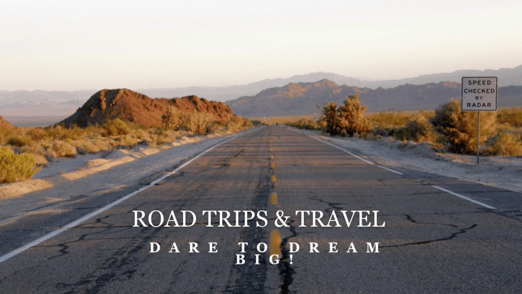 An empty desert road stretches towards the horizon with mountains in the background. Text overlay reads 'ROAD TRIPS & TRAVEL' and 'DARE TO DREAM BIG!'